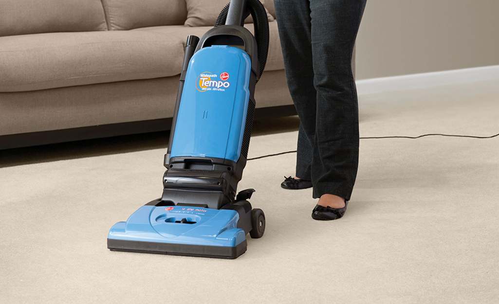 A person pushing an upright vacuum cleaner along the carpet.