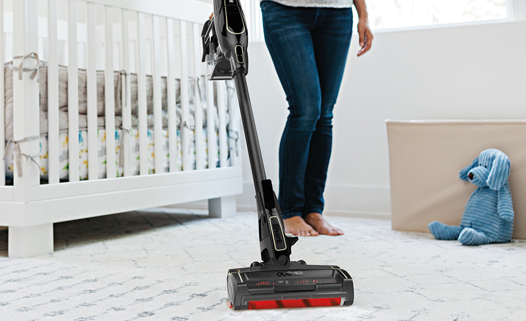 A person pushing a cordless stick vacuum cleaner along a nursery carpet.