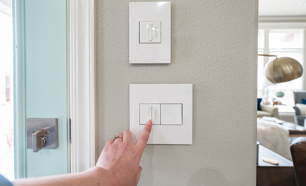 A person touching a single plate wall switch.