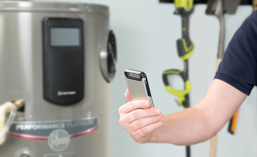 A person programs a smart water heater from a cell phone. A person programs a smart water heater from a cell phone.