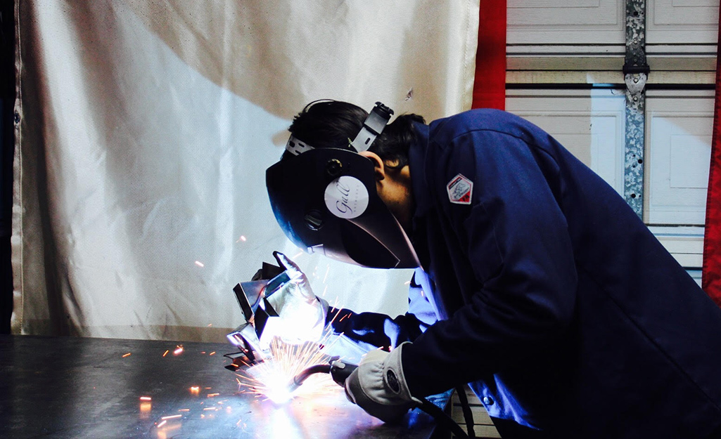 A man is welding in front of a welding blanket.