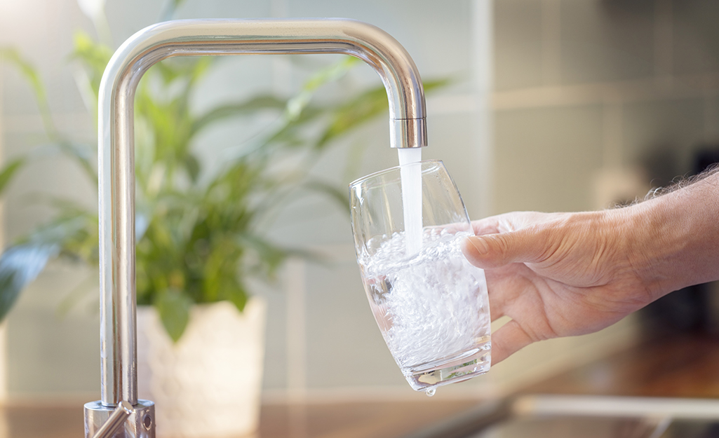 A person filling a glass of water from a kitchen tap.