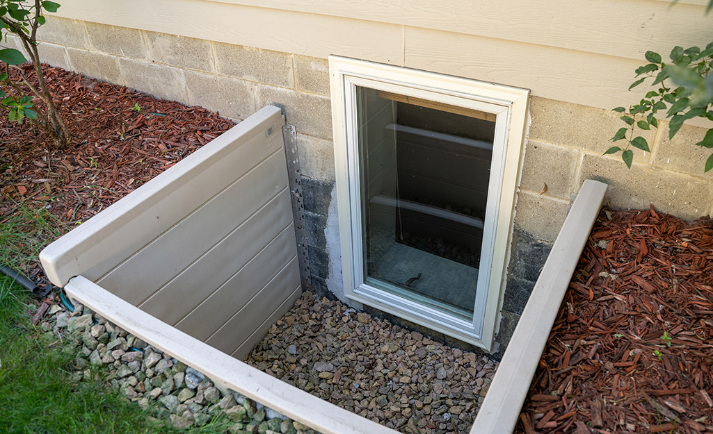 A basement window can be seen in the cinder block foundation of a house.