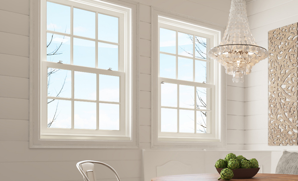 A crystal chandelier hangs over a table in front of a wall of shiplap with windows in aluminum window frames. 