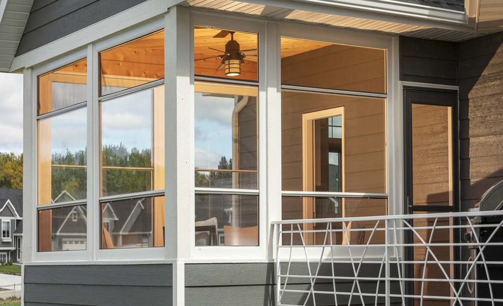 Three walls of double hung windows form a small glassed-in porch that extends from the side of a house.