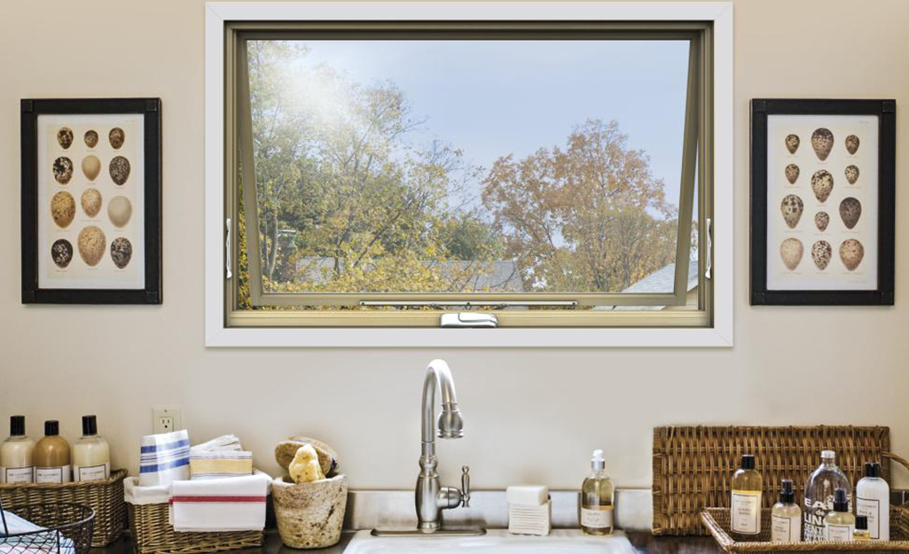 An awning window opens from the bottom above a sink and next to baskets of hand towels and cleaning products.