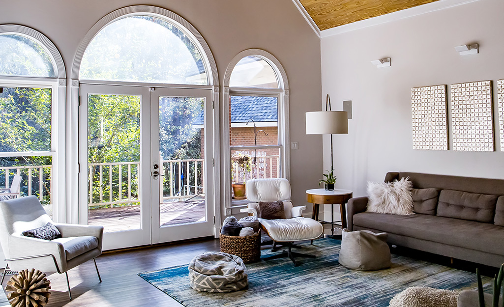 Windows shaped like half circles are installed above two windows and a set of glass doors that lead to a deck from a living room.