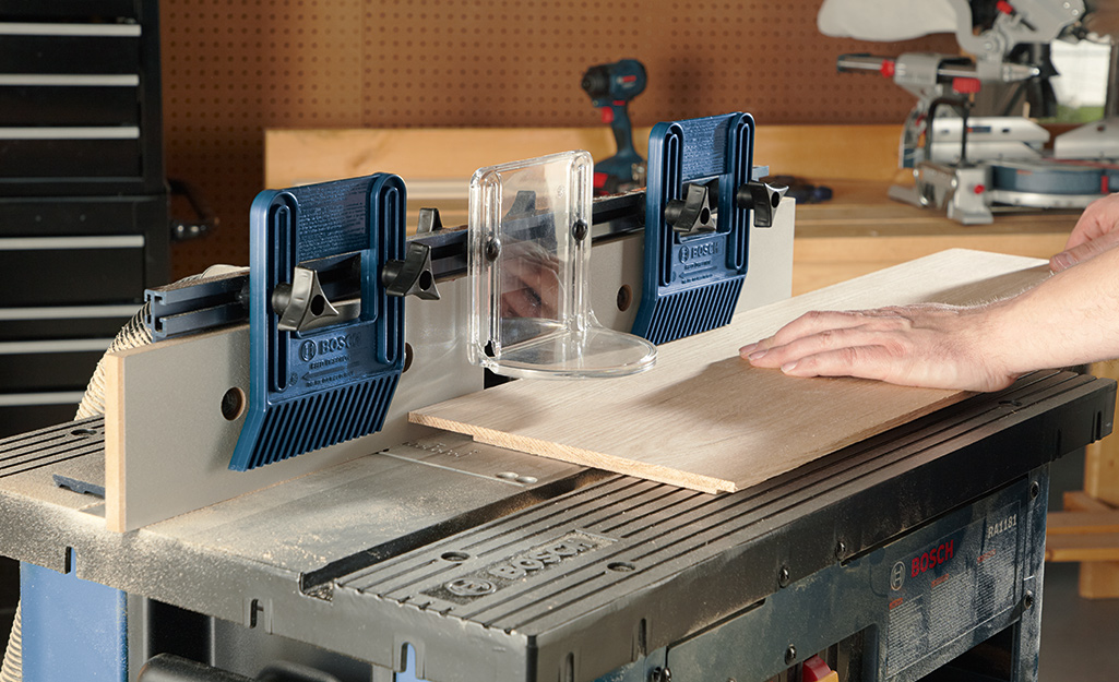 A person stands at a wood router table to use a wood router tool.