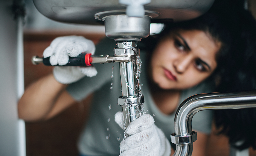 Someone fixing a leaky pipe with a wrench.