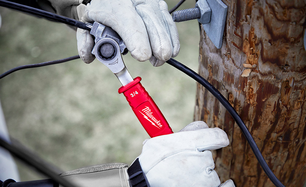 A person using a box wrench on a wire.