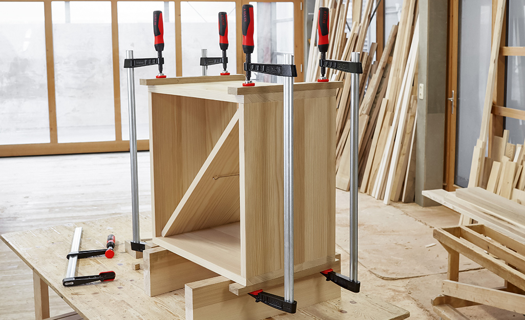 A cabinet in a workshop with clamps holding wood together.