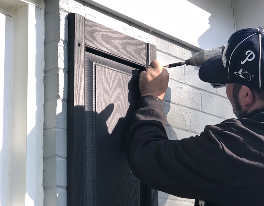 A man installs new black panel shutters on a home.