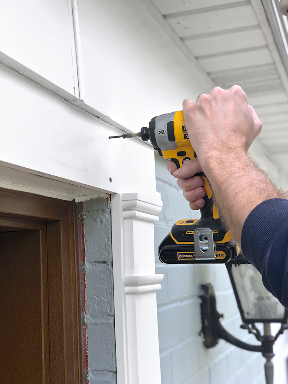 A person using a cordless drill to add trim to the outside of a front door.