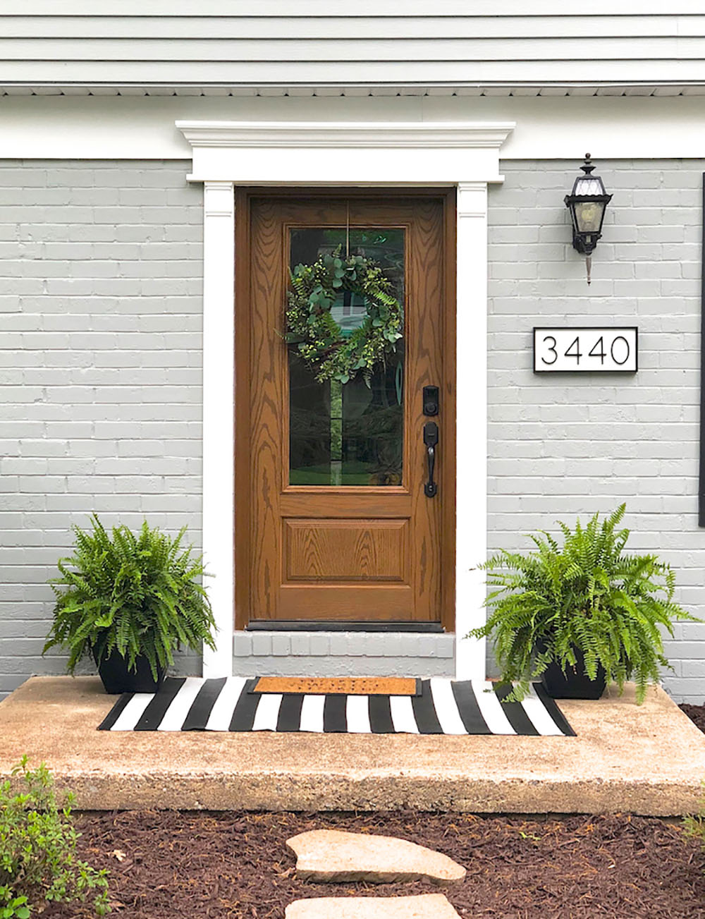 A black and white striped doormat sitting in front of a new front door with new hardware, trim and painted brick.