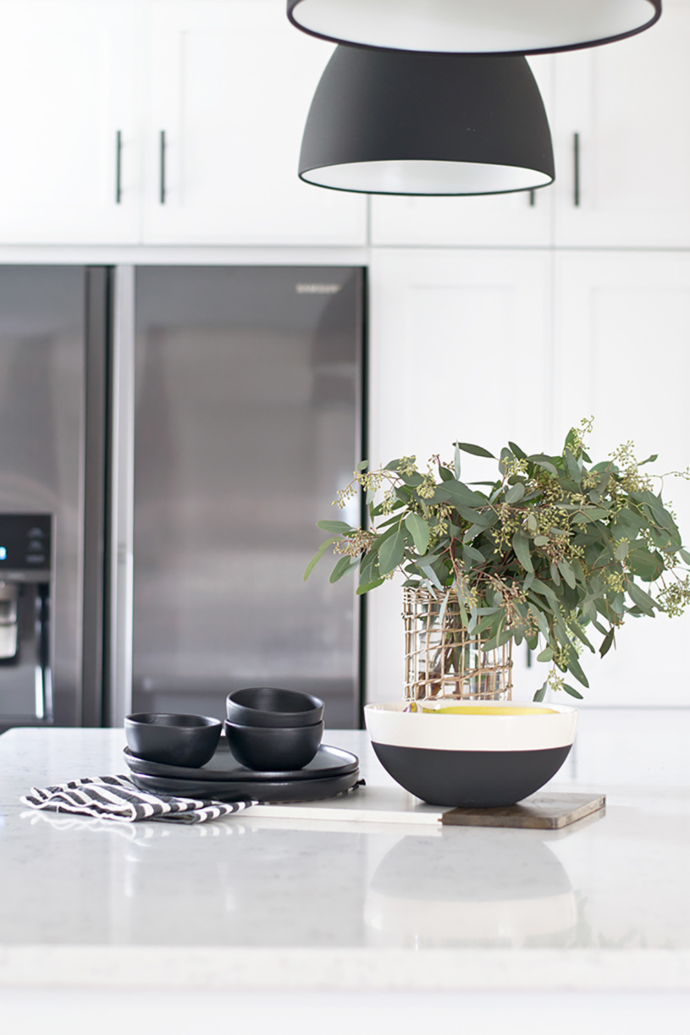 A white quartz countertop decorated with black dishes and greenery.