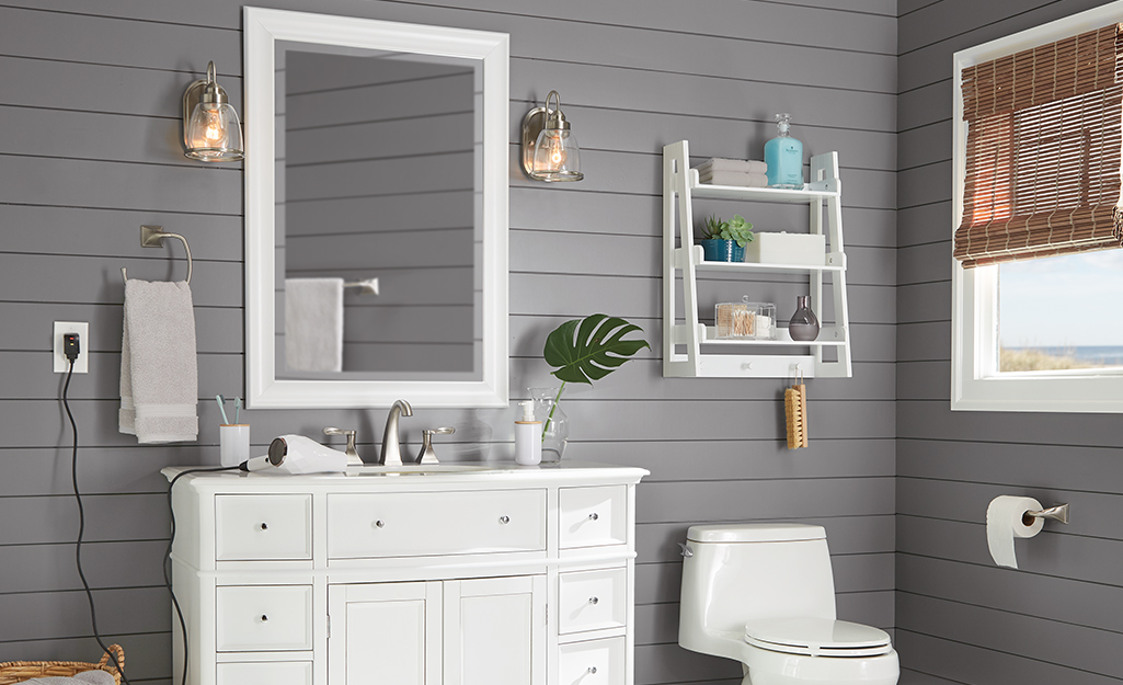 A glass sconce hangs on each side of a mirror in a bathroom with gray shiplap walls and a white vanity.