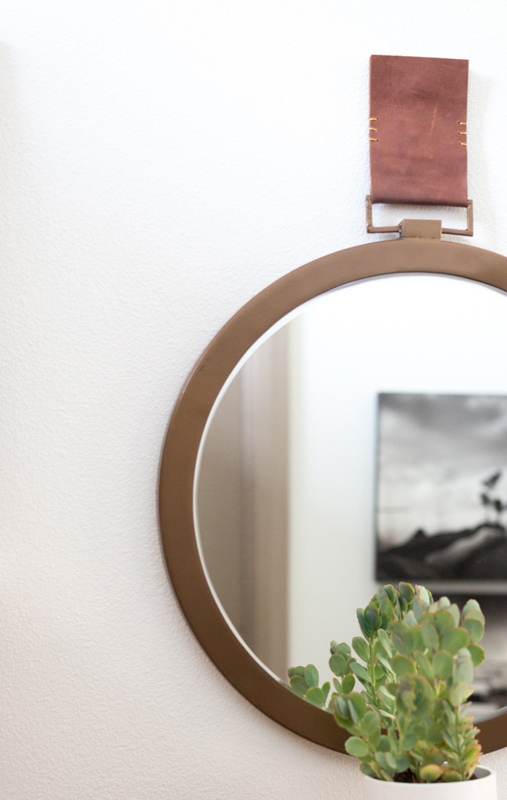 A round iron framed mirror hanging from a leather strap. A round iron framed mirror hanging from a leather strap.