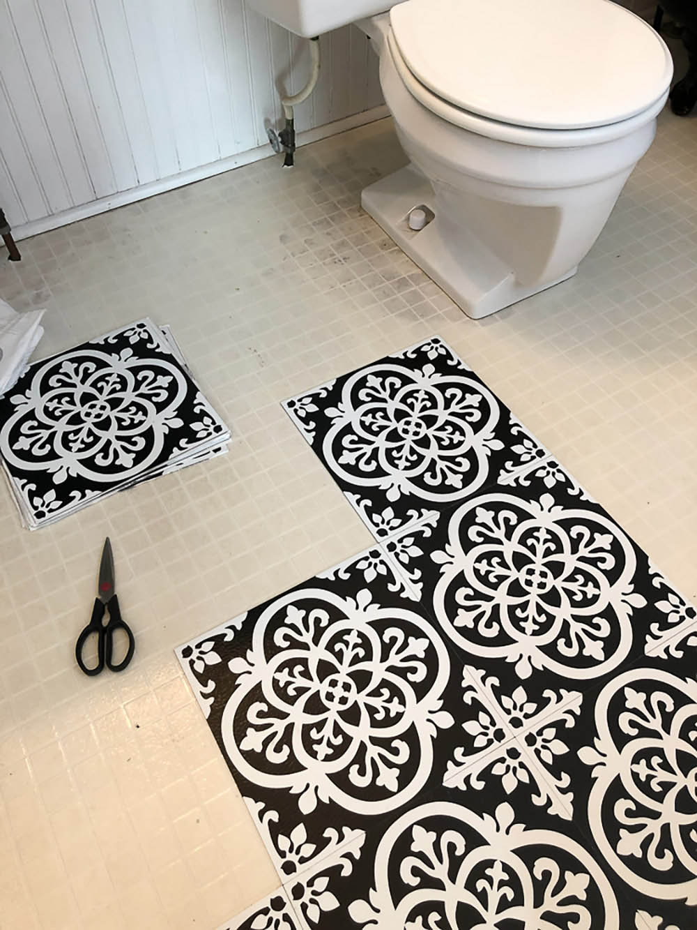 A bathroom floor is covered with white and black peel and stick vinyl floor tiles.