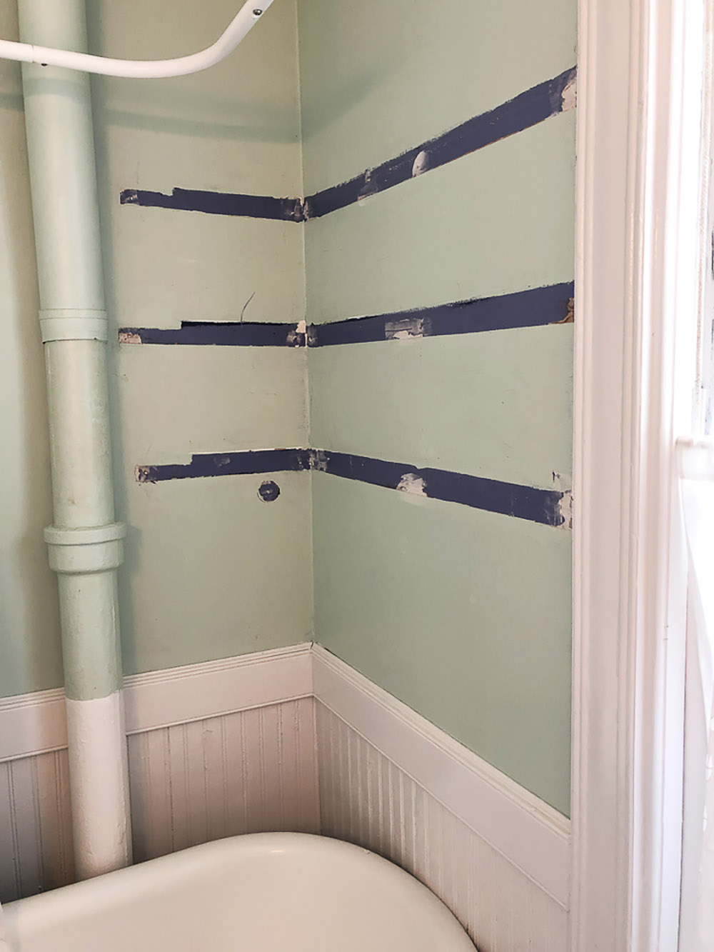 A light green wall with blue paint strips from shelving being removed.