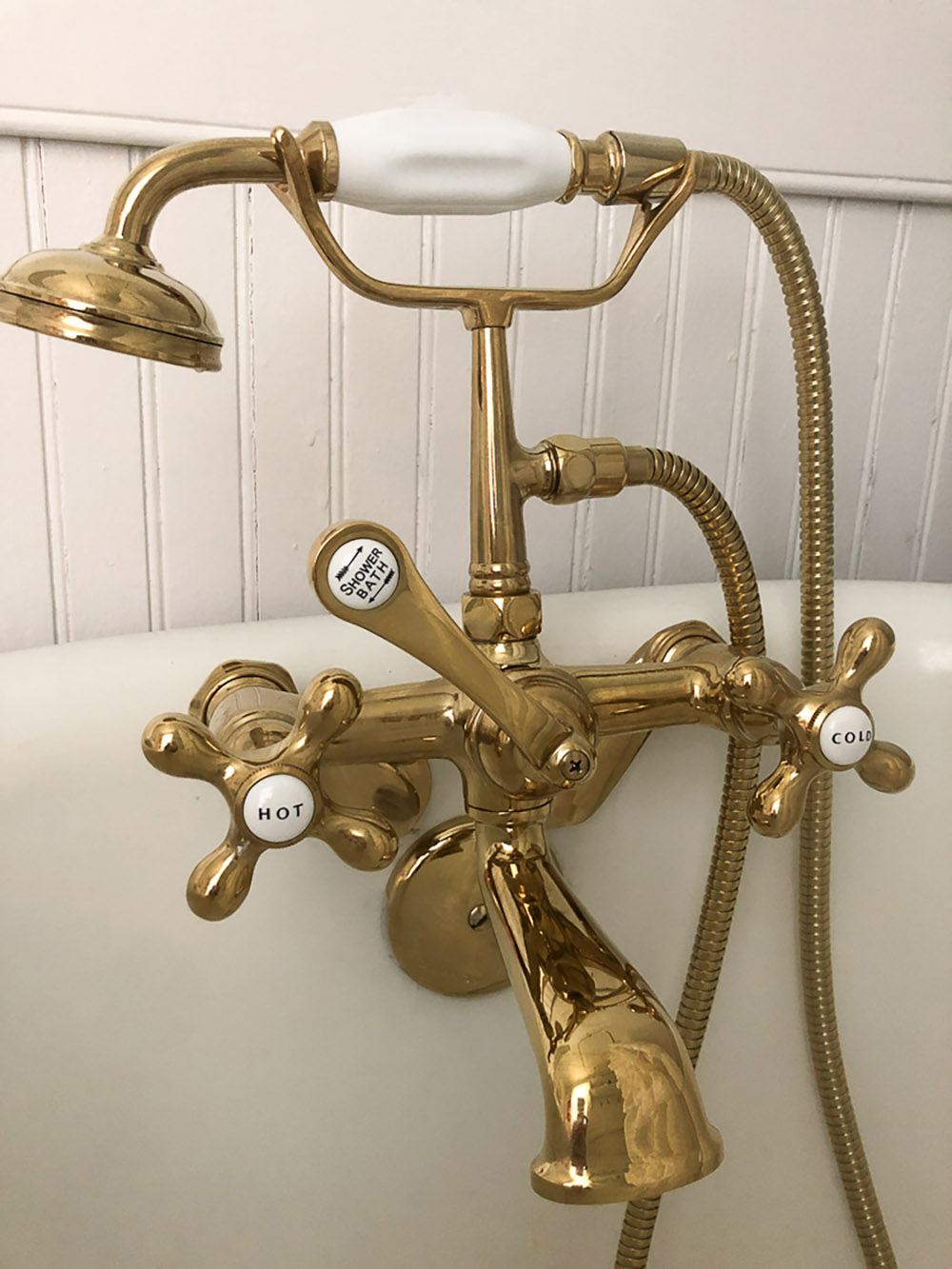 A brass vintage clawfoot tub faucet with a hand shower.