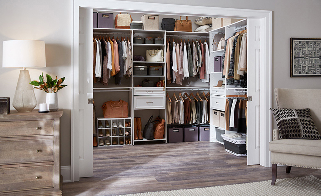 The doors to large walk-in closet stand open to show an organized closet system than includes rods, drawers and shelves.