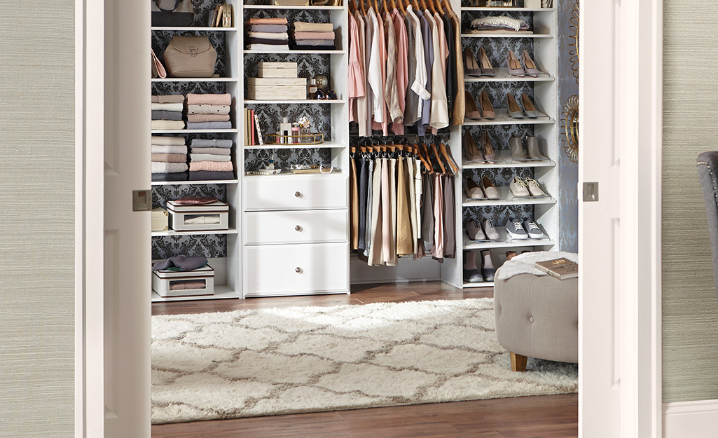 A patterned white rug covers the floor in front of the shelves, drawers and racks of a large walk-in closet.