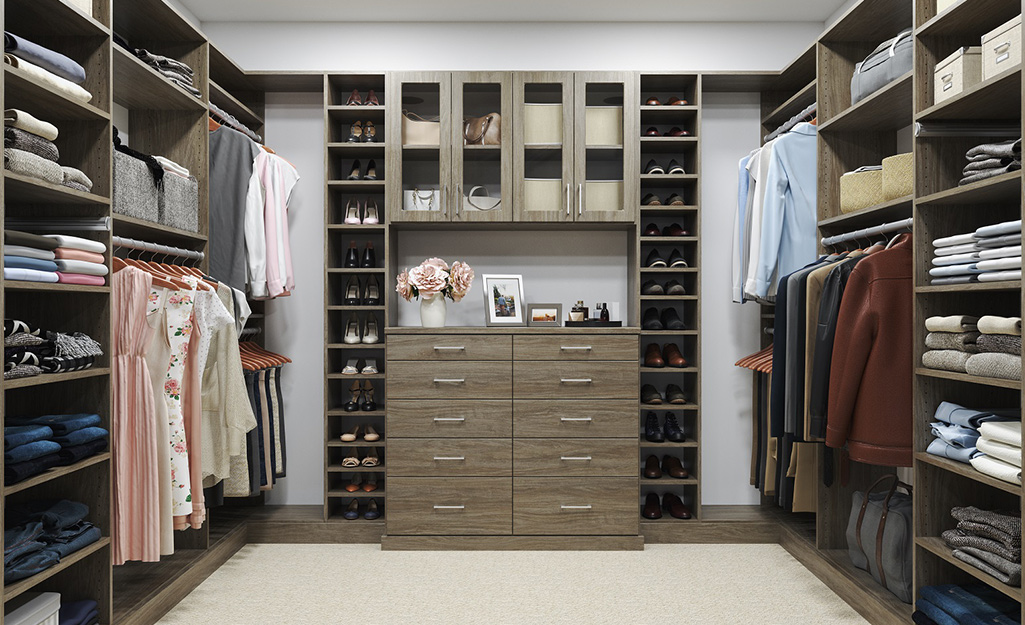 Women’s clothes hang on one side of a walk-in closet, with men’s clothes on the other and shelves and drawers in the back.