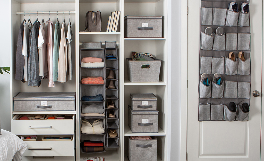 In a walk-in closet, gray bins, boxes and an over-the-door shoe rack provide storage options.