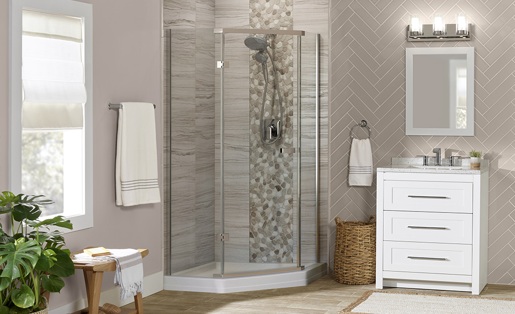 A bathroom with a corner walk-in shower with a clear glass door and tiled walls.