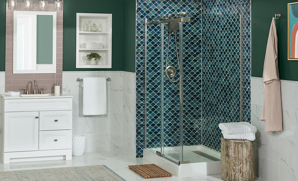 A bathroom with a walk-in shower with clear glass doors and two walls tiled in a colorful pattern. 