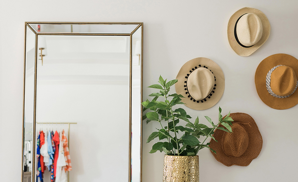 A group of straw hats hung beside a mirror as wall art.