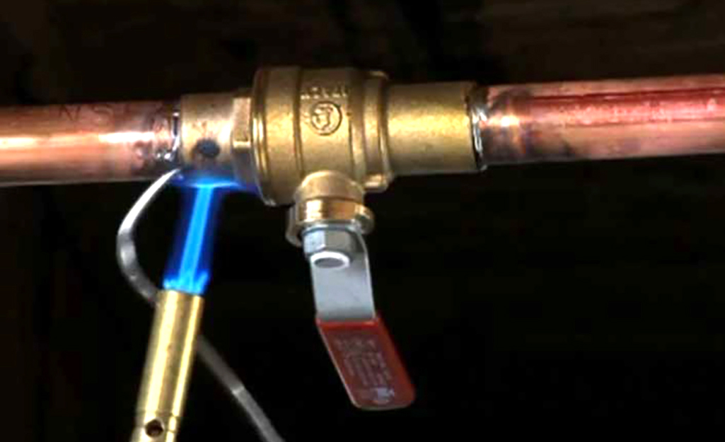 A torch is used to reseal the shutoff valve on water heater piping    