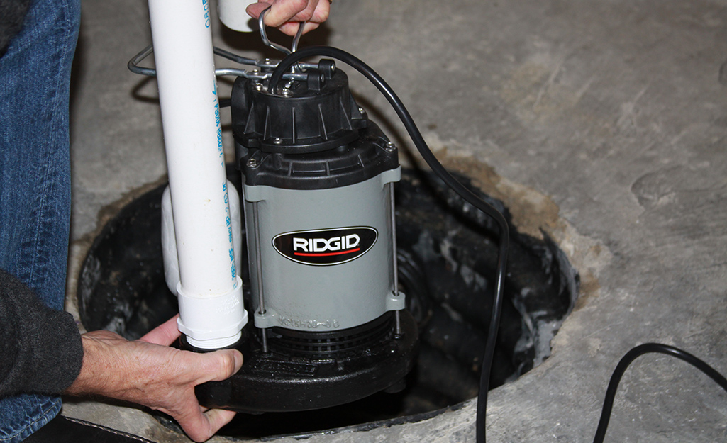 A submersible sump pump being placed in a basement drain.