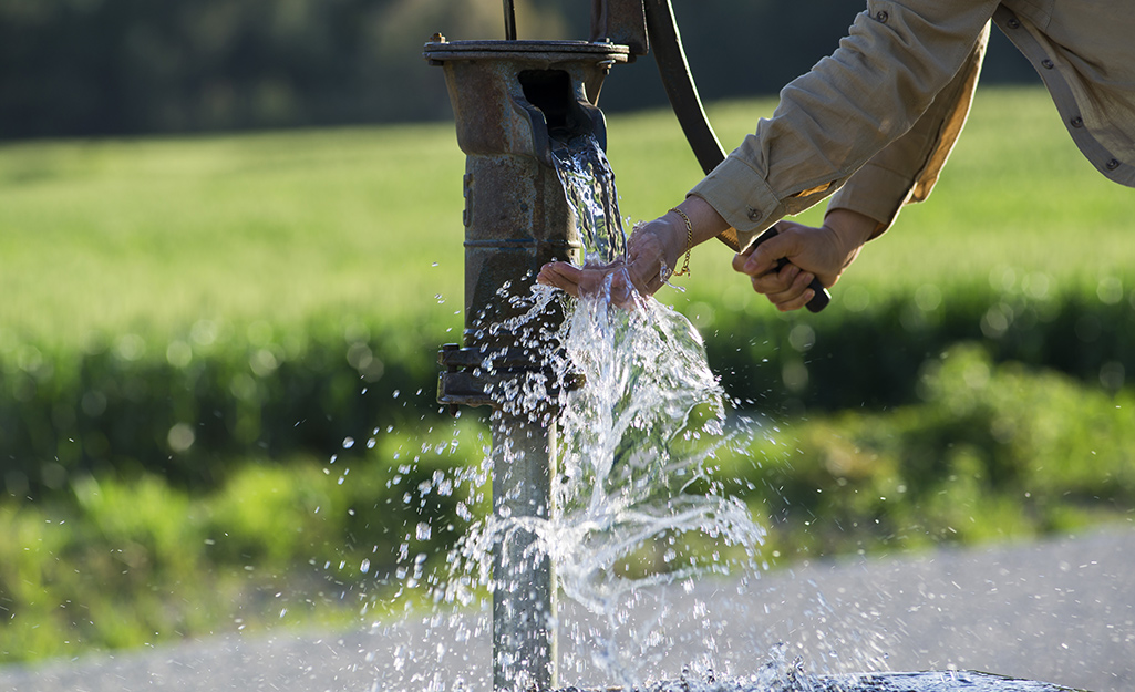 Someone using a hand pump at a well.