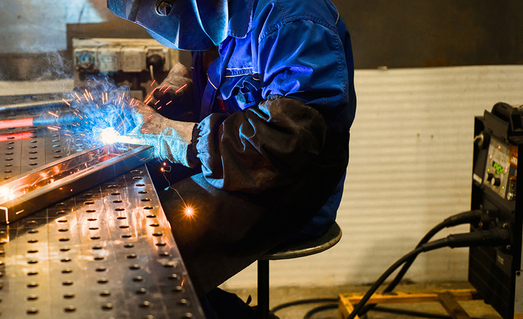 A person welds metal in a workshop.