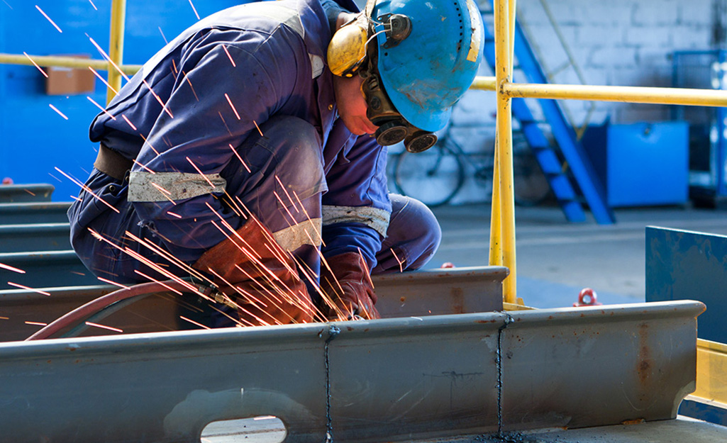 A person kneels down while welding metal.