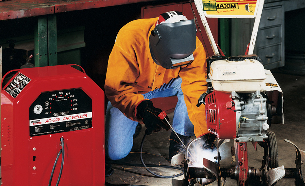 A person kneels down while welding a piece of equipment.