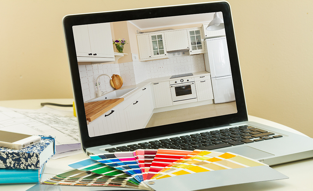 A laptop, paint samples and other kitchen planning tools on a table.