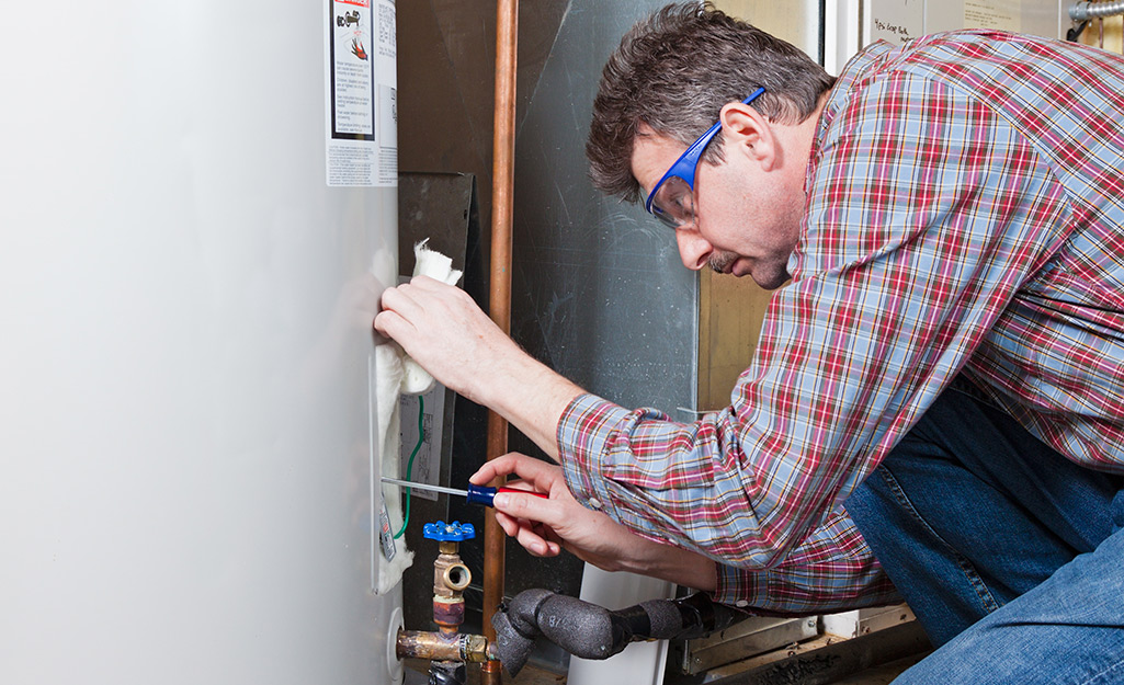 A man wearing safety glasses uses a screwdriver as he works on a water heater.