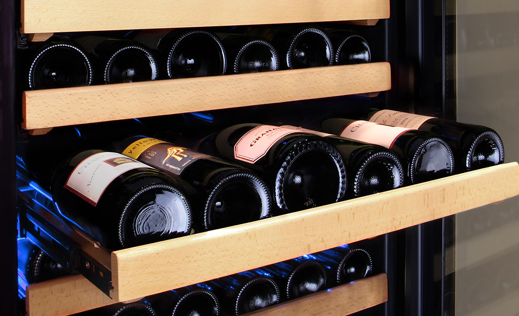Six bottles of wine laying on a shelf inside a wine cooler.