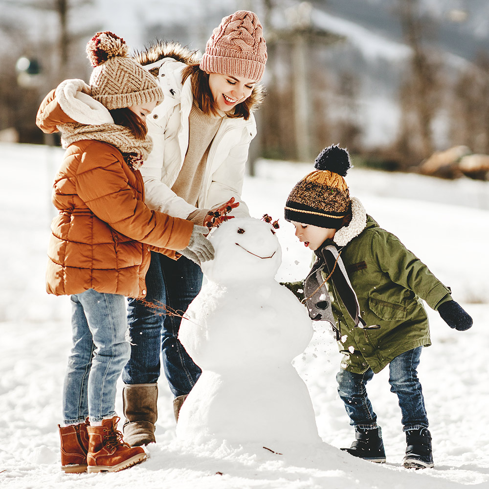 Mom and kids build a snowman in front yard.