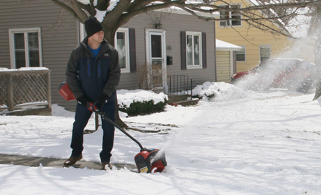 Man using snowblower in driveway.