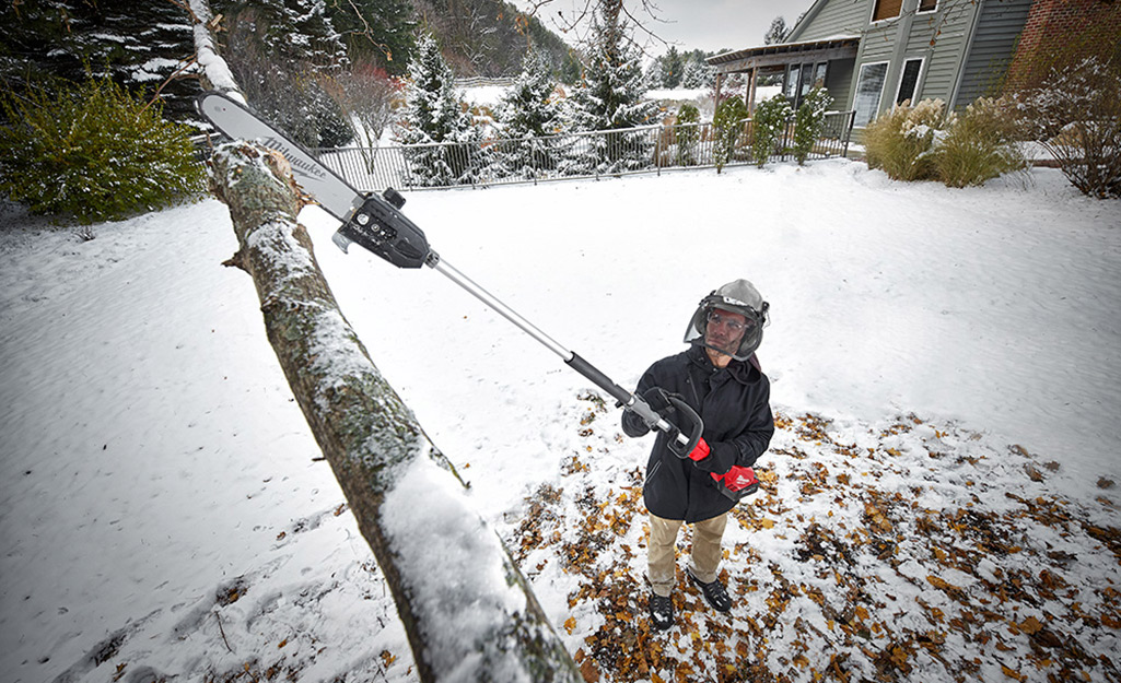 Man using a pole saw to remove a limb in winter.