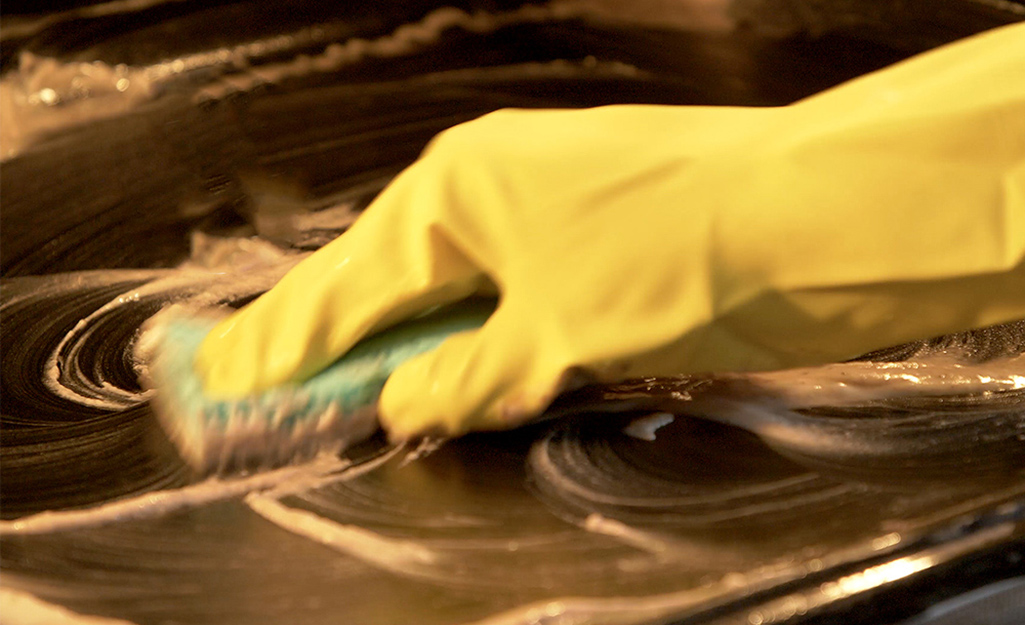 A person scrubs a treated surface in an oven. A person scrubs a treated surface in an oven.
