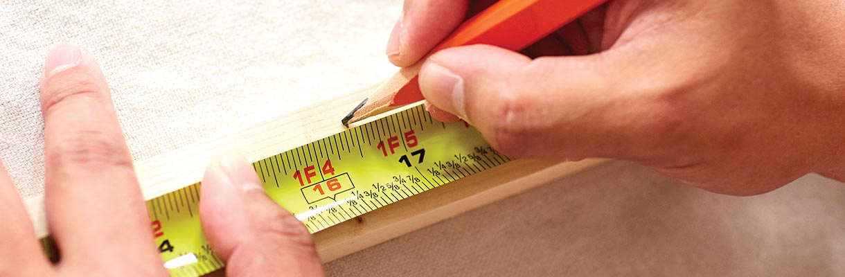Someone marking a spot on a piece of wood using a tape measure. Someone marking a spot on a piece of wood using a tape measure.