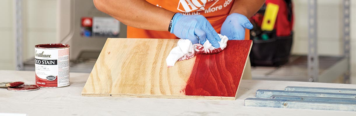 A man using a rag to stain a piece of wood red. A man using a rag to stain a piece of wood red.