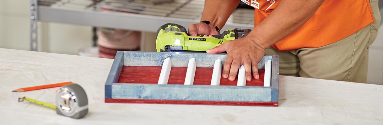 A man using a drill to attach white shelves into a blue and red shelving unit. A man using a drill to attach white shelves into a blue and red shelving unit.