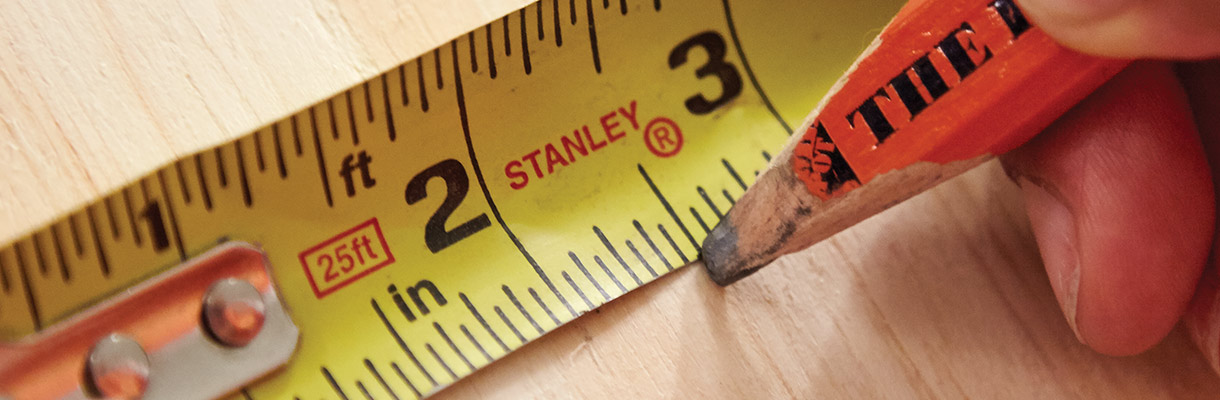 Someone marking a piece of lumber at 2 1/2 inches according to a measuring tape. Someone marking a piece of lumber at 2 1/2 inches according to a measuring tape.