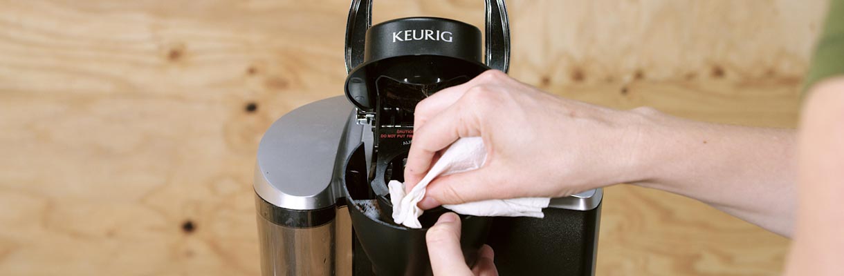 Someone wiping the inside of a Keurig coffee maker Someone wiping the inside of a Keurig coffee maker