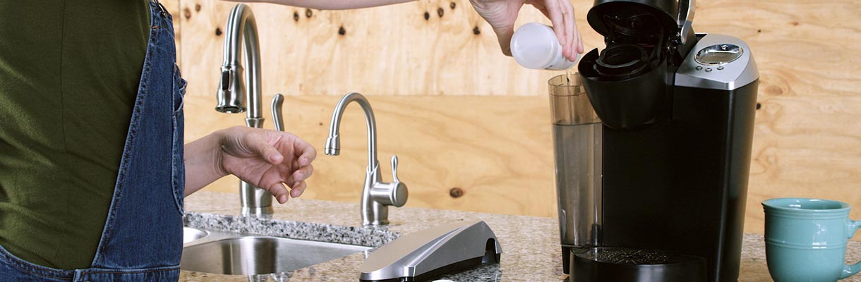 Someone pouring cleaning solution into the water tank of a Keurig Someone pouring cleaning solution into the water tank of a Keurig